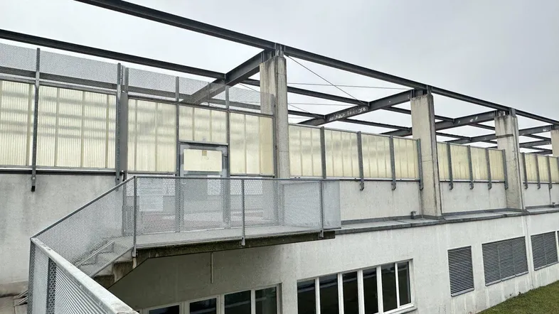 Außenansicht eines Gebäudes mit Metalltreppe und Gitterstrukturen, die zu einer oberen Ebene führen.