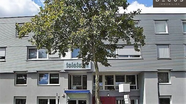 Modernes Mehrfamilienhaus mit vielen Fenstern und einer gepflegten Fassade, umgeben von einem Baum.