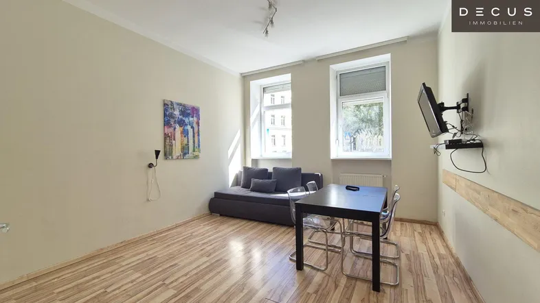 Helles Wohnzimmer mit Holzboden, Sofa, Esstisch und Wandfernseher.