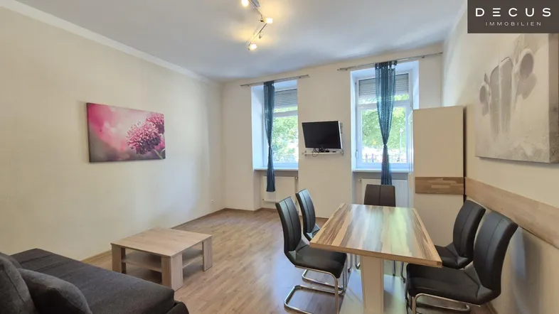 Helles Wohn- und Esszimmer mit Holztisch, Sofa und zwei Fenstern, ausgestattet mit Laminatboden.