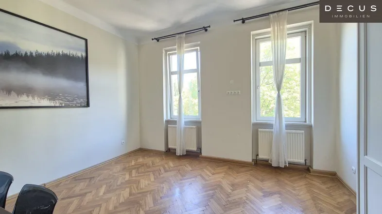 Helles Zimmer mit Fischgrätparkett und großen Fenstern, ideal als Wohnbereich nutzbar.