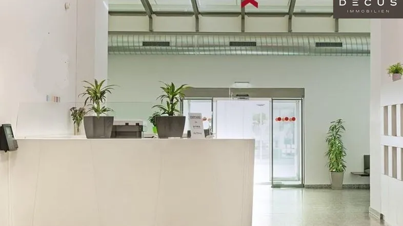 Heller Empfangsbereich mit hohen Decken, Fliesenboden und automatischen Glastüren in einem Bürogebäude.