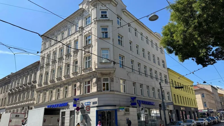 Historisches Eckgebäude mit Geschäften im Erdgeschoss an einer belebten städtischen Straße.