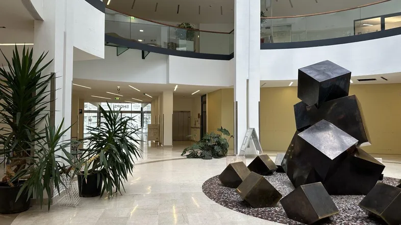 Großzügige, helle Lobby mit Marmorboden, Pflanzen und einer modernen Skulptur, die mehrere Etagen verbindet.
