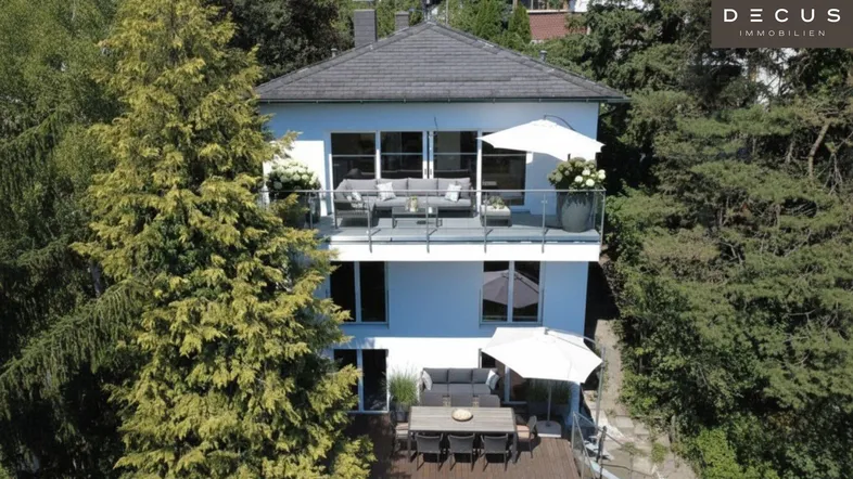 Modernes Wohnhaus mit mehreren Balkonen und Terrassen, umgeben von üppigem Grün und hohen Bäumen.