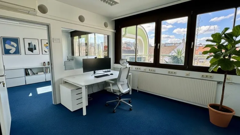 Modernes Büro mit blauem Teppichboden, großen Fenstern und Blick auf die Stadt.