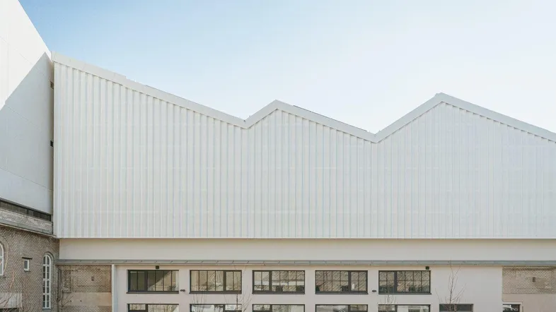 Moderne Architektur mit markantem Sägezahndach und großen Fensterfronten im Erdgeschoss des Gebäudes.