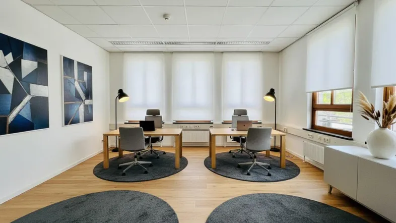 Modernes Büro mit zwei Arbeitsplätzen, Holzboden und großen Fenstern, die viel Tageslicht hereinlassen.