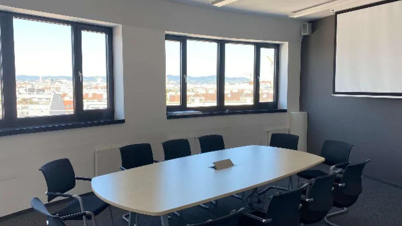 Heller Konferenzraum mit großem Tisch, Projektor und weitem Stadtblick durch die Fenster.