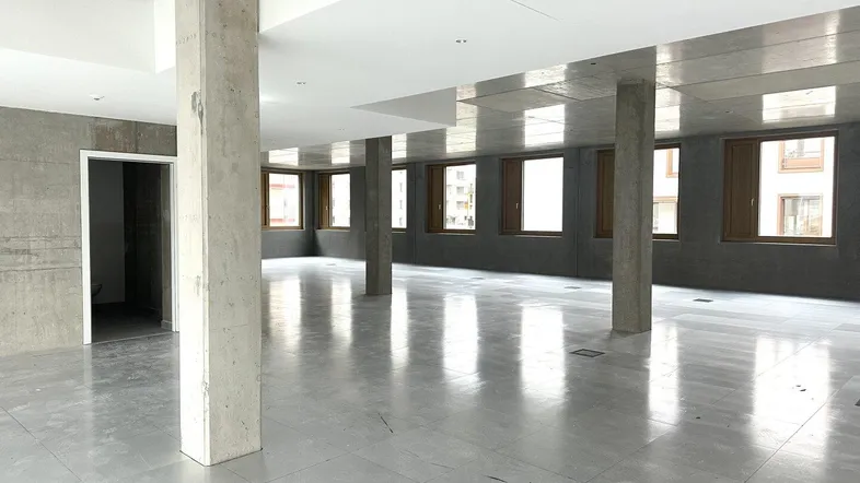 Geräumiger, offener Büroraum mit hohen Decken, großen Fenstern und modernem Betonboden.