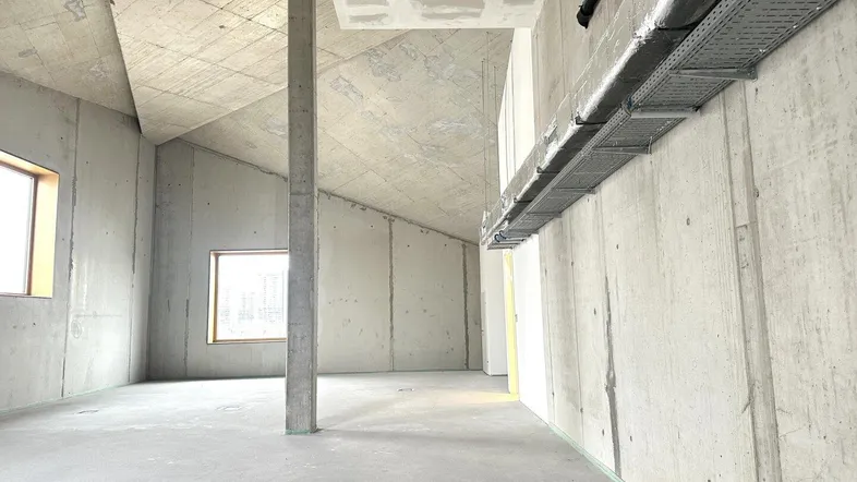 Großer, unfertiger Innenraum mit Betonwänden und -decken, hohen Decken und sichtbaren Installationen.