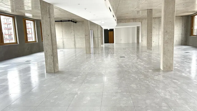 Geräumiger, unmöblierter Büroraum mit Sichtbetonwänden und großen Fenstern, bereit für den Ausbau.