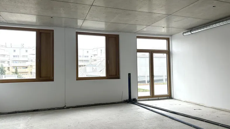 Leerer Raum mit Betonboden, unverputzten Wänden und großen Fenstern, bereit für den Ausbau.