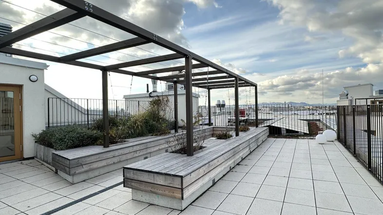 Geräumige Dachterrasse mit Holzdecks, Pflanzbeeten und einer modernen Pergola-Struktur unter bewölktem Himmel.