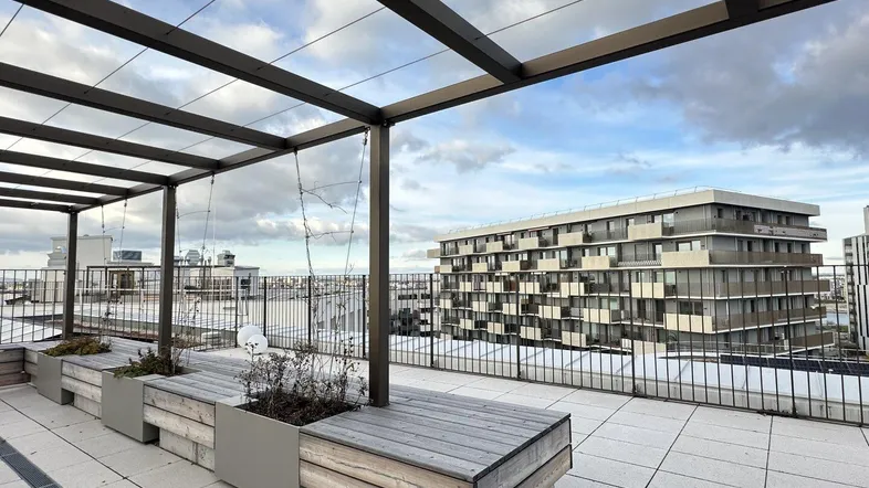 Geräumige Dachterrasse mit Holzbänken und Blick auf die umliegenden Gebäude unter bewölktem Himmel.