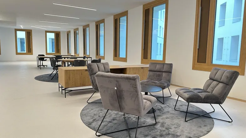 Großer, offener Bürobereich mit modernen Sitzgelegenheiten, langen Fenstern und integrierter Beleuchtung.