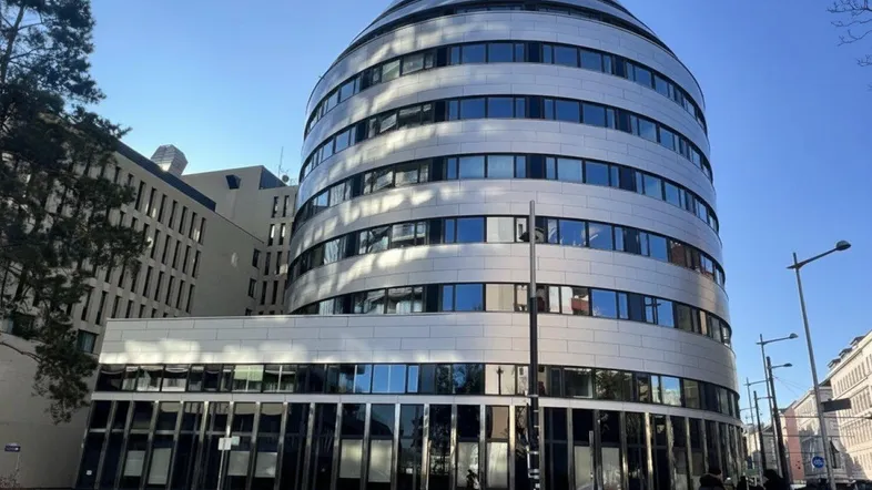 Modernes Bürogebäude mit geschwungener Fassade und vielen Fenstern unter blauem Himmel.