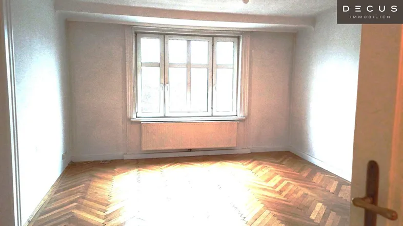 Heller Raum mit Fischgrätparkett und großem Fenster, ideal als Wohn- oder Schlafzimmer.