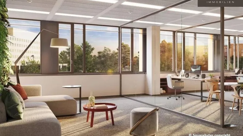 Moderner Büroraum mit Lounge-Bereich und Arbeitsplätzen, durch Glaswände getrennt, mit großen Fenstern und viel Tageslicht.