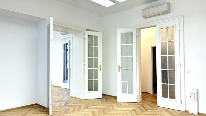 Geräumiger Raum mit Fischgrätparkett, Flügeltüren und Klimaanlage, ideal für Büro oder Wohnen.