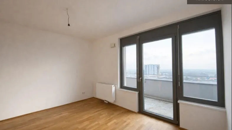 Helles Zimmer mit Parkettboden, großen Fenstern und Zugang zu einem kleinen Balkon mit Stadtblick.