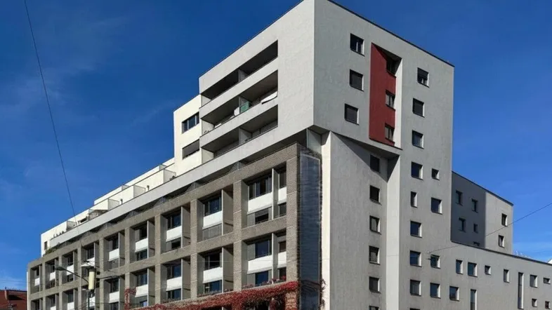 Moderne Wohnanlage mit markanter Architektur, verschiedenen Fassadenfarben und Balkonen unter blauem Himmel.