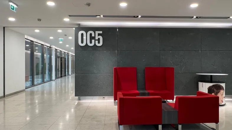Moderner Empfangsbereich mit roten Sitzgelegenheiten und Fliesenboden in einem Bürogebäude.