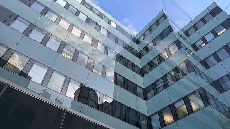 Moderne Bürogebäude-Fassade mit vielen Fenstern und spiegelnden Oberflächen unter blauem Himmel.
