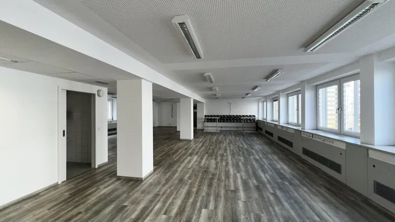 Geräumiger, leerer Büroraum mit vielen Fenstern, Säulen und modernem Laminatboden, bereit zur individuellen Gestaltung.