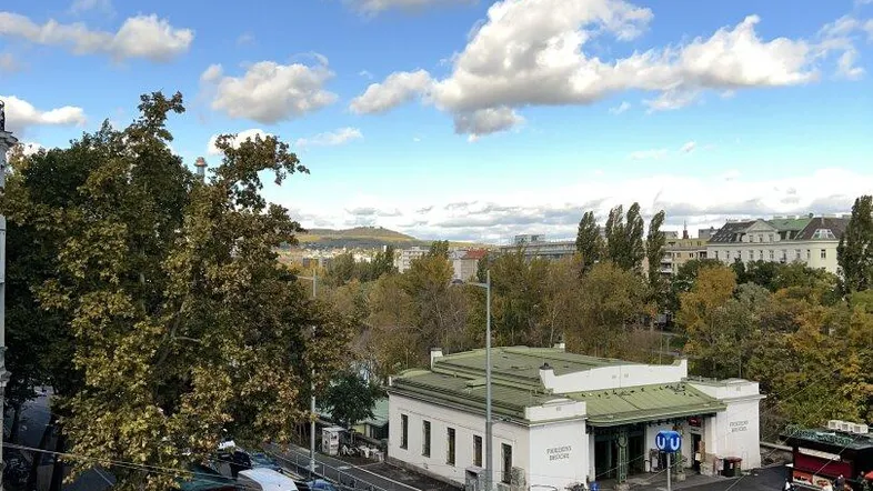 Blick aus dem Fenster auf eine belebte Straße, ein historisches Gebäude und grüne Hügel in der Ferne.