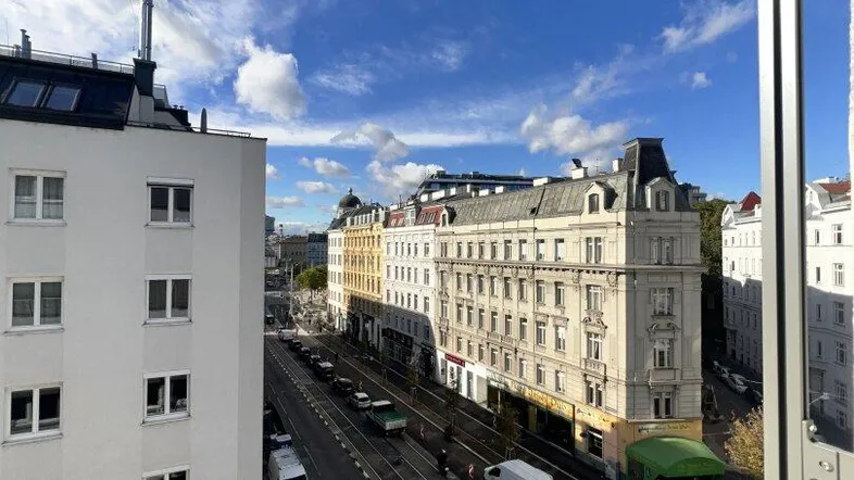 Weitblick über eine belebte Stadtstraße mit historischen Gebäuden unter einem blauen Himmel.