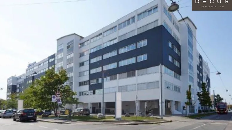 Modernes Bürogebäude mit weißer und dunkelblauer Fassade an einer Straßenecke mit Parkplätzen.