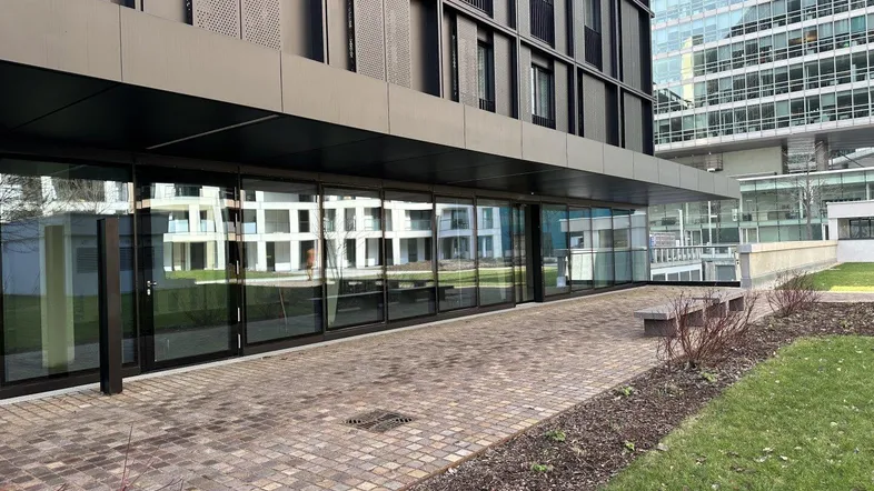 Moderne Gebäudefassade mit großen Glasfronten und gepflastertem Gehweg vor dem Eingangsbereich.