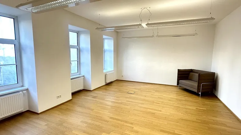 Geräumiger Büroraum mit hellem Parkettboden, großen Fenstern und moderner Deckenbeleuchtung.