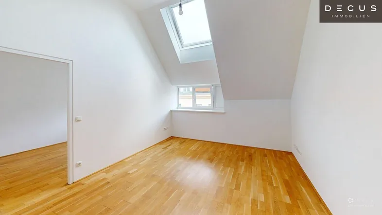 Helles Zimmer im Dachgeschoss mit Holzboden, Dachschrägen und einem Dachfenster für viel Tageslicht.