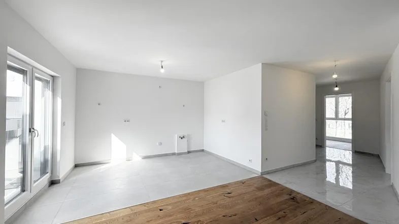 Heller, unmöblierter Wohnbereich mit Parkettboden und Zugang zu einem Balkon oder einer Terrasse.