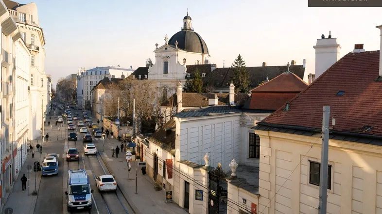 Panoramablick auf eine belebte Stadtstraße mit historischen Gebäuden und einer Kirche im Hintergrund.