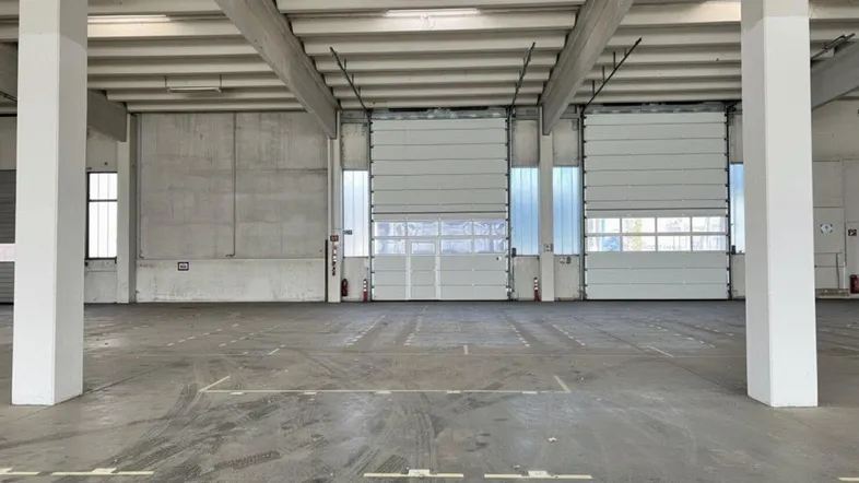 Große Lagerhalle mit Betonboden, hohen Decken und zwei Rolltoren für LKW-Zugang.