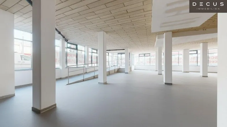 Geräumiger, heller Gewerberaum im Rohbau mit hohen Decken, großen Fenstern, Säulen und einer Rampe.