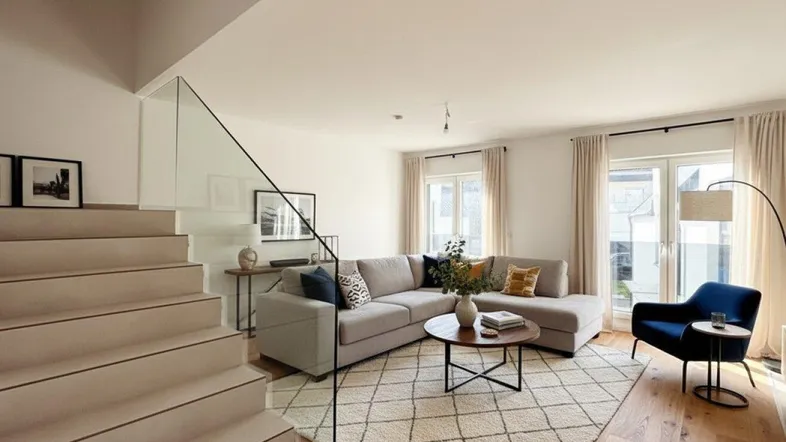 Helles Wohnzimmer mit modernem Sofa, Holzboden und offener Treppe mit Glasgeländer.