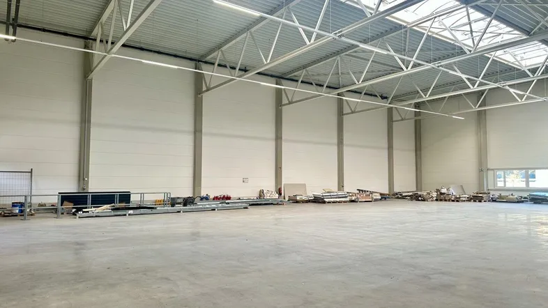 Geräumige Lagerhalle mit hoher Decke, Oberlichtern und Betonboden, bereit für die Nutzung.