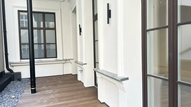 Eine moderne Terrasse mit Holzboden und Kiesbett, umgeben von einer weißen Fassade mit großen Fenstern.
