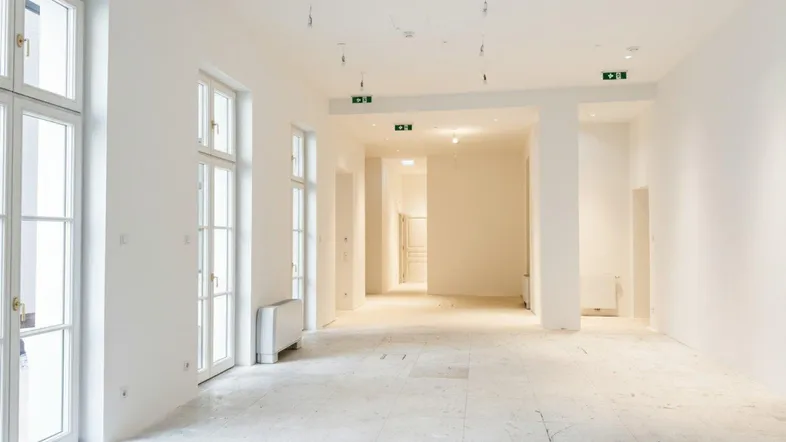 Großer, heller Raum mit hohen Fenstern und hellem Steinboden, ideal für Büronutzung in einem Altbau.