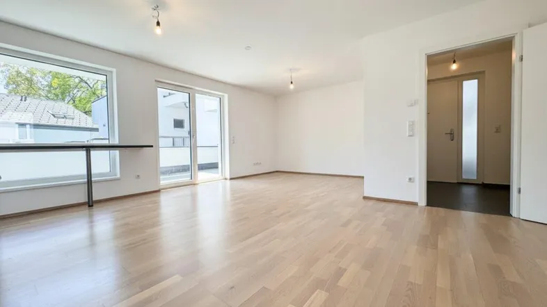 Geräumiger Wohnbereich mit hellem Parkettboden und großzügigem Zugang zum Balkon.