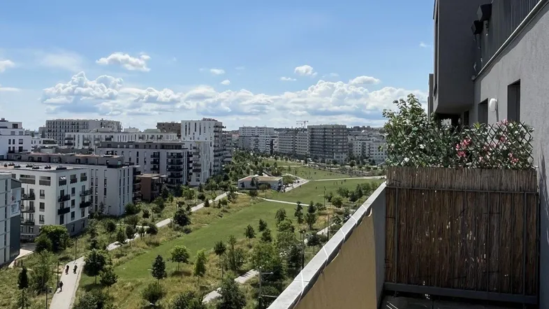 Blick vom Balkon auf eine weitläufige Grünfläche mit modernen Wohngebäuden im Hintergrund.