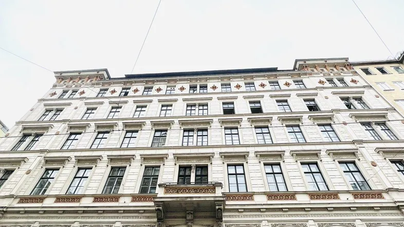 Klassische Fassade eines Altbaus mit vielen Fenstern und einem kleinen Balkon.
