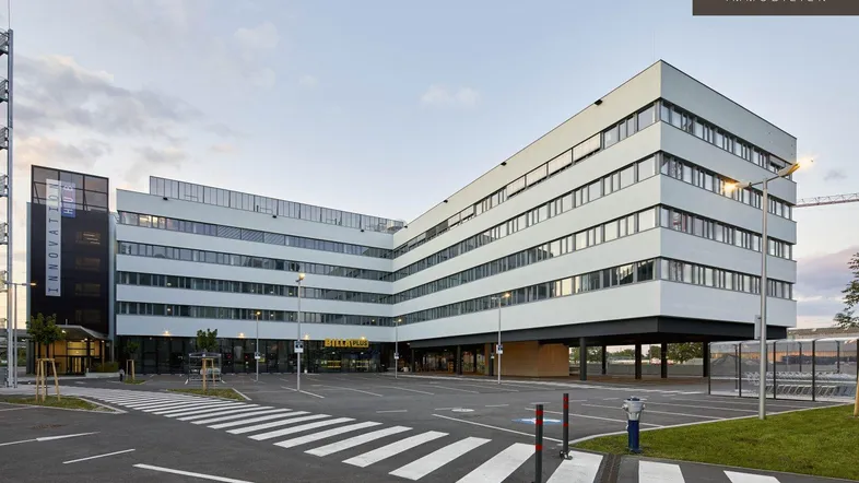 Modernes Bürogebäude mit markanter Architektur, großen Fenstern und ausreichend Parkplätzen im Freien.