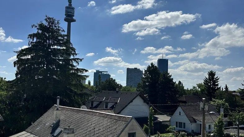 Panoramablick über die Dächer der Stadt mit dem Donauturm im Hintergrund unter blauem Himmel.