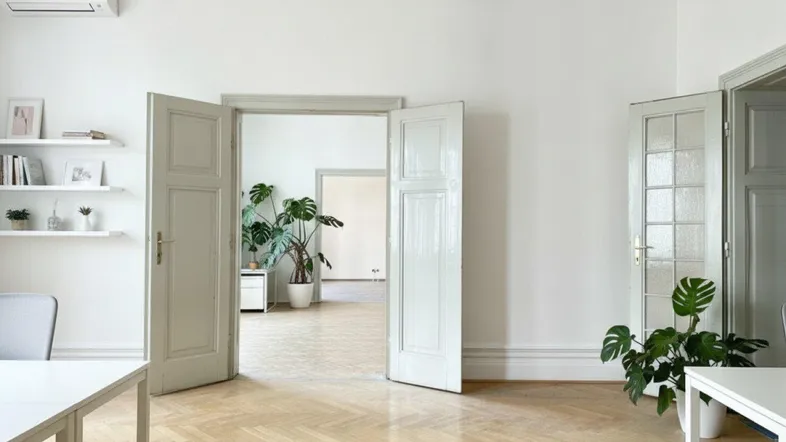 Helles Büro mit Fischgrätparkett, weißen Wänden und Blick in angrenzende Räume.