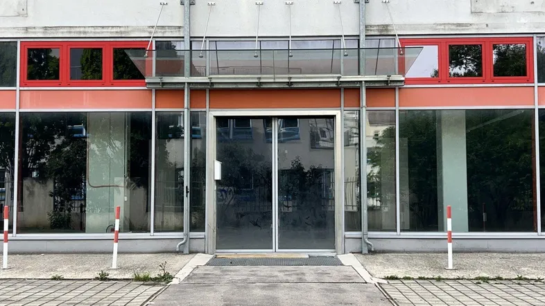 Eingangsbereich eines Geschäftsgebäudes mit großen Glasfronten und roten Fensterrahmen.